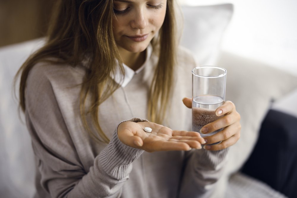 Person holding pill and glass of water.
