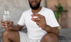 CloseupOfYoungBlackManSittingOnBedWithGlass